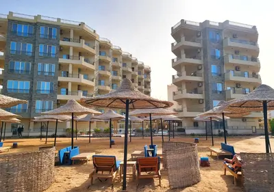 a beach with chairs and umbrellas in front of a building at La Quinta Beach Resort Hurghada in Hurghada