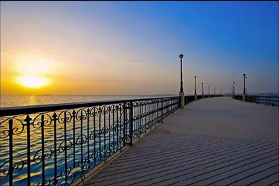 a boardwalk leading to the beach with the sun setting at Luxury Apartment In Azzurra Sahl Hashish 6G101 in Hurghada