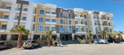 a large building with palm trees in front of it at Relax near the sea, one bedroom flat in Hurghada
