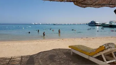a beach with people in the water and boats at Tiba Golden Resort in Hurghada