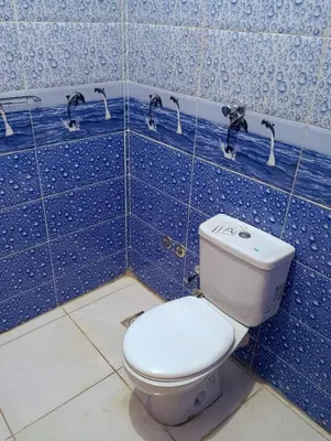 a blue tiled bathroom with a toilet and faucets at Lutos flower apartment 2 in Al Karnak