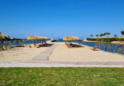 a beach with straw umbrellas and chairs and the water at Balkan Beach Resort- Relaxing Beach Apartment in Hurghada