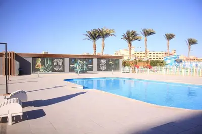 a swimming pool with two white chairs and palm trees at Scandic Resort in Hurghada