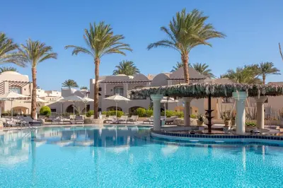 a large swimming pool with palm trees and buildings at Iberotel Makadi Beach in Hurghada
