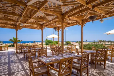 a restaurant with wooden tables and chairs and the beach at The Cascades Golf Resort, Spa & Thalasso in Hurghada