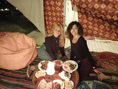 two women sitting on a bed with plates of food at Nuba Narty in Aswan