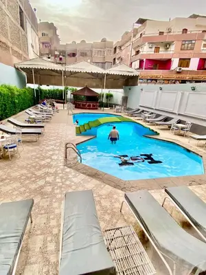 a large swimming pool with chairs and a man in the background at Shady Hotel Luxor in Luxor