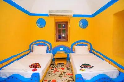 two beds in a room with yellow walls at Nubian Palace Eco Lodge - A Nubian Home Since 1959 in Aswan