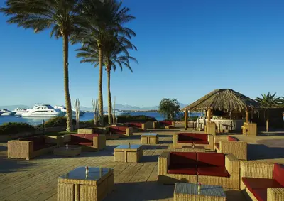 a row of tables and chairs on a beach with palm trees at Hurghada Suites & Apartments Serviced by Marriott in Hurghada