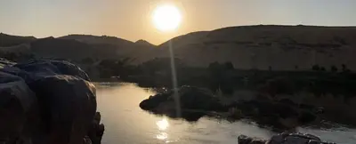 a river with the sun setting in the background at El Prince Guesthouse in Aswan