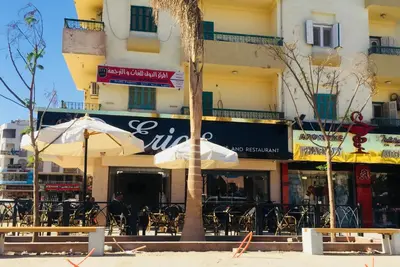 an outdoor cafe with tables and umbrellas in front of a building at Lima Modern Sheraton with Wi Fi in Hurghada