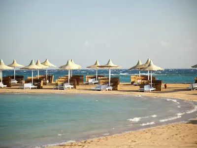 a beach with umbrellas and chairs and the ocean at Hurghada Coral Beach Hotel in Hurghada