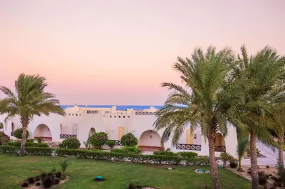 a building with palm trees in front of it at Hilton Marsa Alam Nubian Resort in Abu Dabab