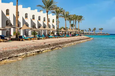 a beach with chairs and umbrellas next to the water at Arabia Azur Resort in Hurghada