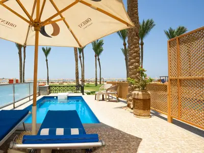 a swimming pool with an umbrella and two blue lounge chairs at Stella Beach Resort & Spa, Makadi Bay in Hurghada