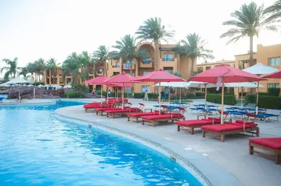 a pool with red chairs and umbrellas next to a resort at Stella Beach Resort & Spa, Makadi Bay in Hurghada