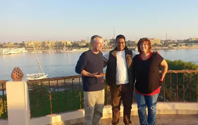 three people standing on a balcony next to the water at Luxor Plaza House in Luxor