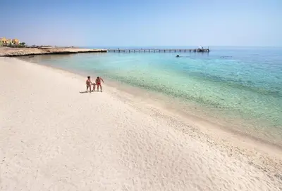 two people walking on a beach near the ocean at Concorde Moreen Beach Resort in Abu Dabab