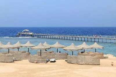 a group of umbrellas on a beach with a pier at Three Corners Happy Life Beach Resort in Abu Dabab