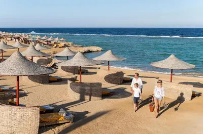 a man and woman walking on a beach with umbrellas at Three Corners Happy Life Beach Resort in Abu Dabab