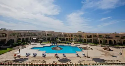 a large courtyard with a pool with chairs and umbrellas at Nubian Village Sky, Hurghada in Hurghada