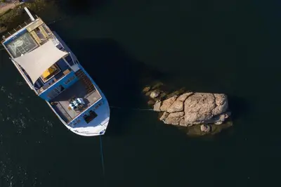 a boat in the water next to a large rock at Anakob in Aswan