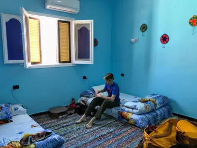 a boy sitting on a bed in a blue room at Nubian Kingdom Aragheed House in Aswan