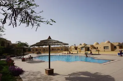 a pool with an umbrella and people sitting around it at Studio at Hurghada- NS2 in Hurghada