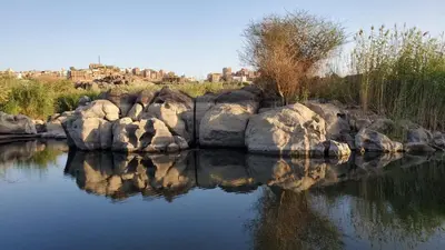 a body of water with rocks and buildings in the background at Adad Noubian House in Aswan