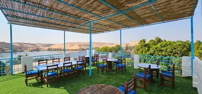 a patio with tables and chairs and a view of the water at Basmatic Nubian Guest House in Aswan