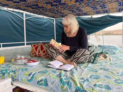 a woman sitting on a boat reading a book at Felucca Sailing Boat Overnight Experience in Aswan