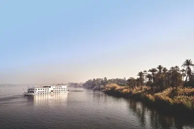 a white boat on a river with palm trees at JAZ Imperial Nile Imperial Cruise - Every Thursday from Luxor- Aswan- Luxor for 07 Nights in Luxor