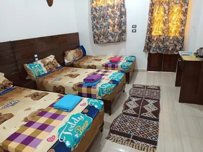 a room with three beds and a table and windows at ABAZIDO Nubian Guest House in Aswan