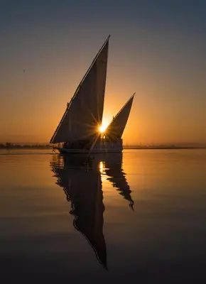 a boat on the water with the sun in the background at Dahabiya ECO Queen Cleopatra in Esna