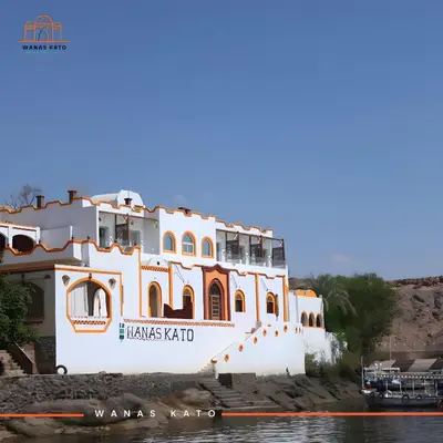 a building on the water with a boat in front at Wanas Kato Guest House in Shellal