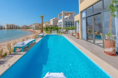 a swimming pool in front of a house next to the water at La Casa de Playa Tawila on Island 4BR Private with Heated Pool in Hurghada