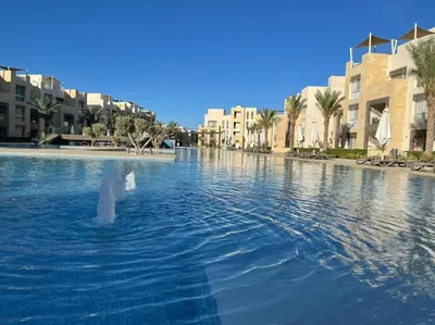 a swimming pool in a resort with palm trees and buildings at Kitesurfer Shared House, Pool View & Beach Access in Hurghada