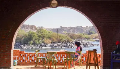 a woman sitting at a table looking out over a river at Artika Wadi Kiki Hotel in Aswan