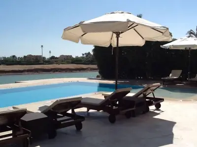 an umbrella and lounge chairs next to a swimming pool at Gorgeous Villa in Gouna with Heated Private Pool in Hurghada