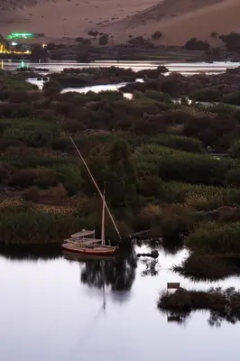 a boat sitting on the water at night at ASWAN NILE PALACE (swimming pool-rooftop-Nile view) in Aswan