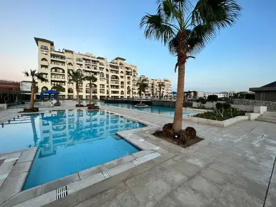a swimming pool with a palm tree in front of a building at AlDAU Heights Modern Brand New Apartments in Hurghada