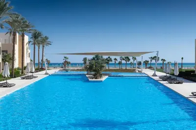 a swimming pool with palm trees and the ocean at Balanced & Bright 2 BDR Mangroovy Free Pool & Beach Access in Hurghada