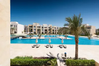 a pool with chairs and a palm tree and buildings at Jazzy 1BDR w Outdoor Pool View Terrace Free Pool & Beach Access in Hurghada