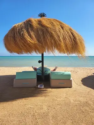 a person laying in a chair under a straw umbrella on the beach at Mangroovy Gouna 1 BR apartment in Hurghada
