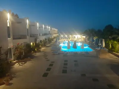 an outdoor swimming pool at night with umbrellas and lights at La Casa Beach in Hurghada