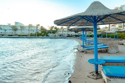 a beach with blue chairs and an umbrella at Royal Star Beach Resort in Hurghada