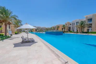 a swimming pool with two lounge chairs and an umbrella at Elegant 2-Bedroom Apartment in Mangroovy, Pool & Beach in Hurghada