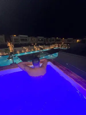 a man laying in a swimming pool at night at Lovely 1 Bedroom with private heated Jacuzzi at Sholan El Gouna in Hurghada