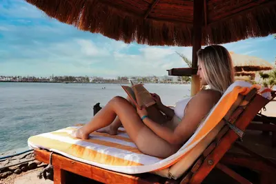 a woman sitting on a beach chair reading a book at New Eagles Downtown Zahabia Resort & Aqua Park in Hurghada