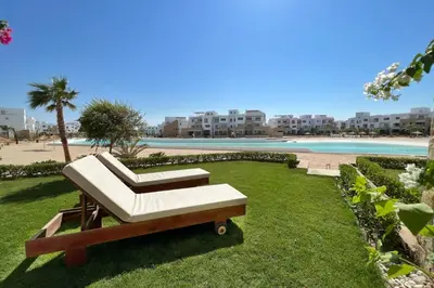 a bench sitting on the grass next to a beach at Lagoonfront Easy 1BDR Swan Lake El Gouna in Hurghada